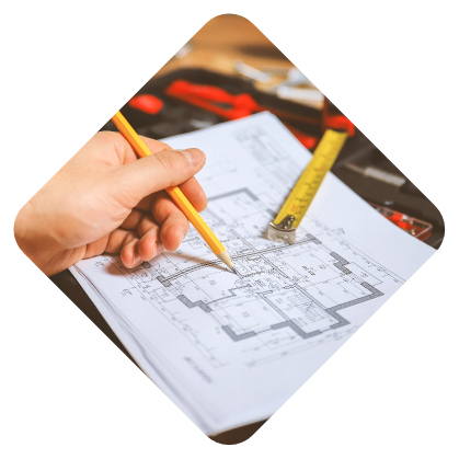 Hand holding a pencil over architectural blueprints with a tape measure in the background