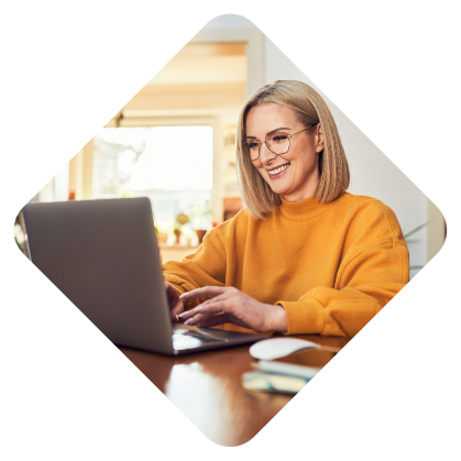 Woman in a yellow sweater smiling while working on a laptop.